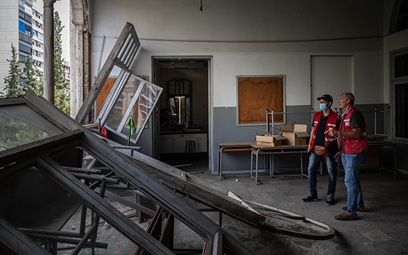 Two experts from the Swiss Humanitarian Aid Unit look out of a broken wall of a classroom.