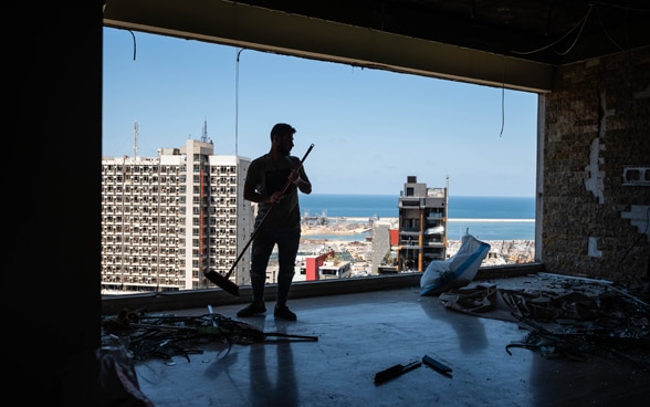 Résident nettoyant un espace de vie détruit dans un immeuble d'appartements surplombant le port de Beyrouth.