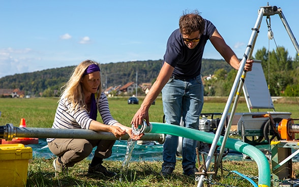 Deux experts soulèvent les conduites d'où s'écoule l'eau.