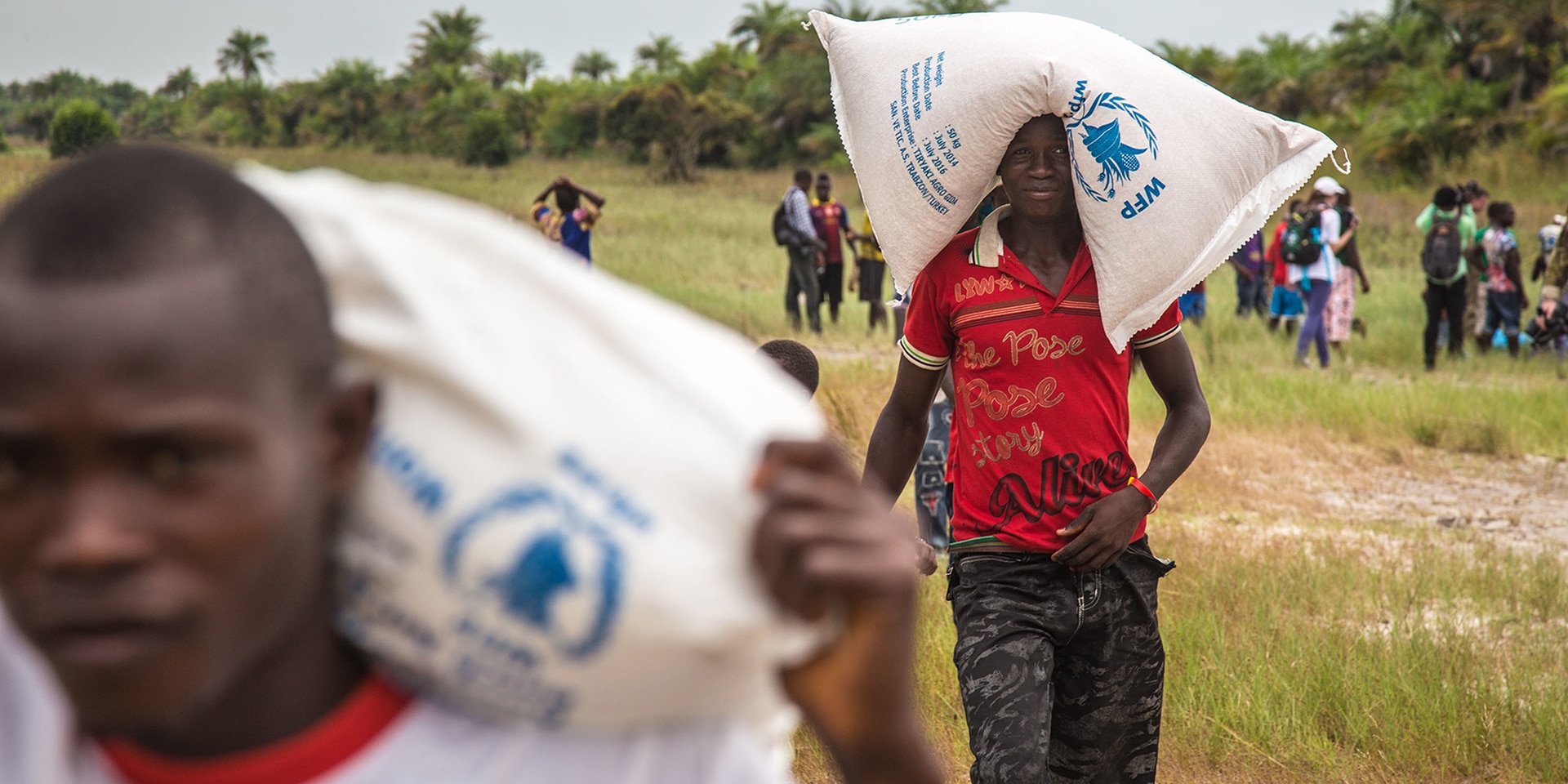  Two men carry bags of food on their shoulders and head.