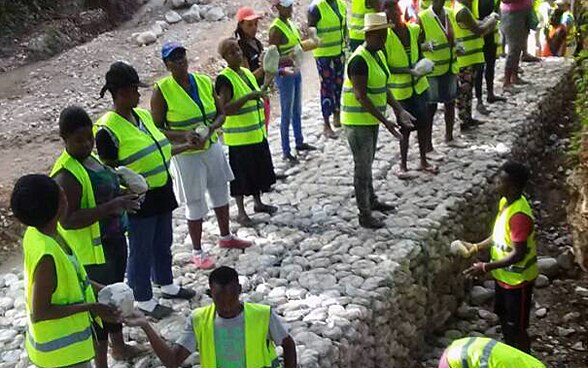 Un gruppo di persone indossa un gilet di sicurezza giallo e sposta delle pietre per costruire dei gabbioni.