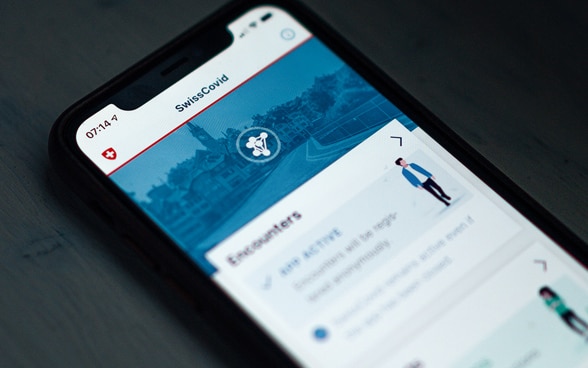 Ein Smartphone auf einem Tisch zeigt die Homepage der SwissCovid-App.