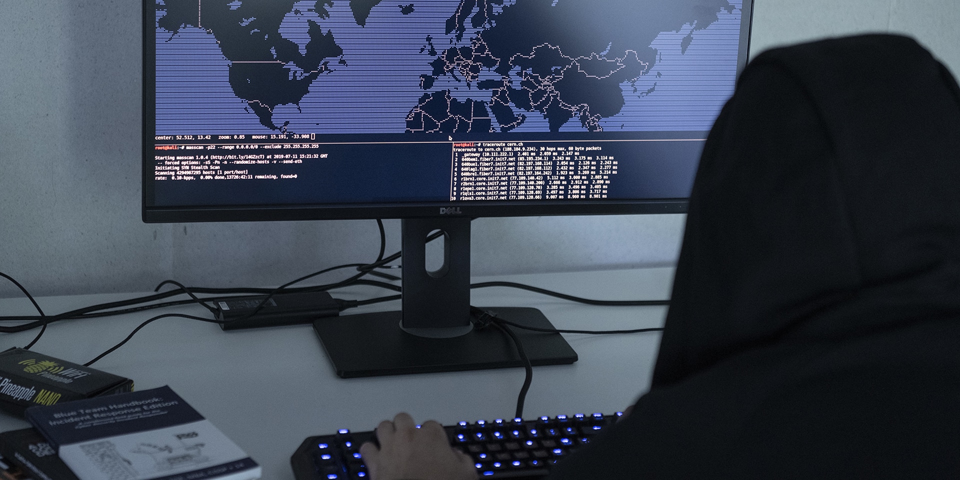 To symbolise cybercrime, a man in a hooded sweatshirt sits in front of a computer displaying a map of the world and modifies programming codes.