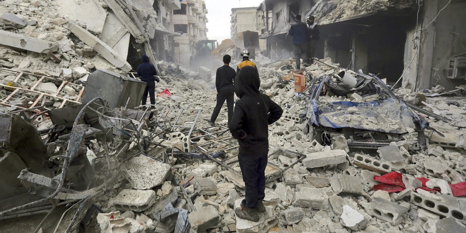 In a street in the town of Idlib, civilians walk through a field of rubble. In the foreground a hooded boy looks into the distance.