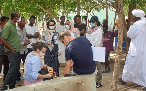 Zwei Experten der Humanitäre Hilfe nehmen Wasserproben. Ein paar Leute stehen um sie herum.