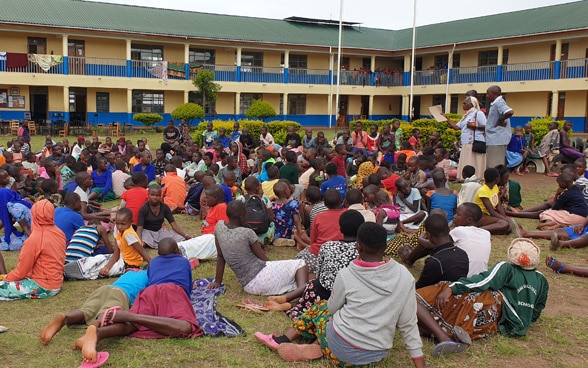 A class of children sit together on a lawn.