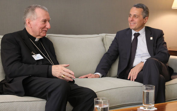 Bundesrat Cassis sitzt mit Kardinal Pietro Parolin auf einem Sofa und unterhält sich mit ihm.