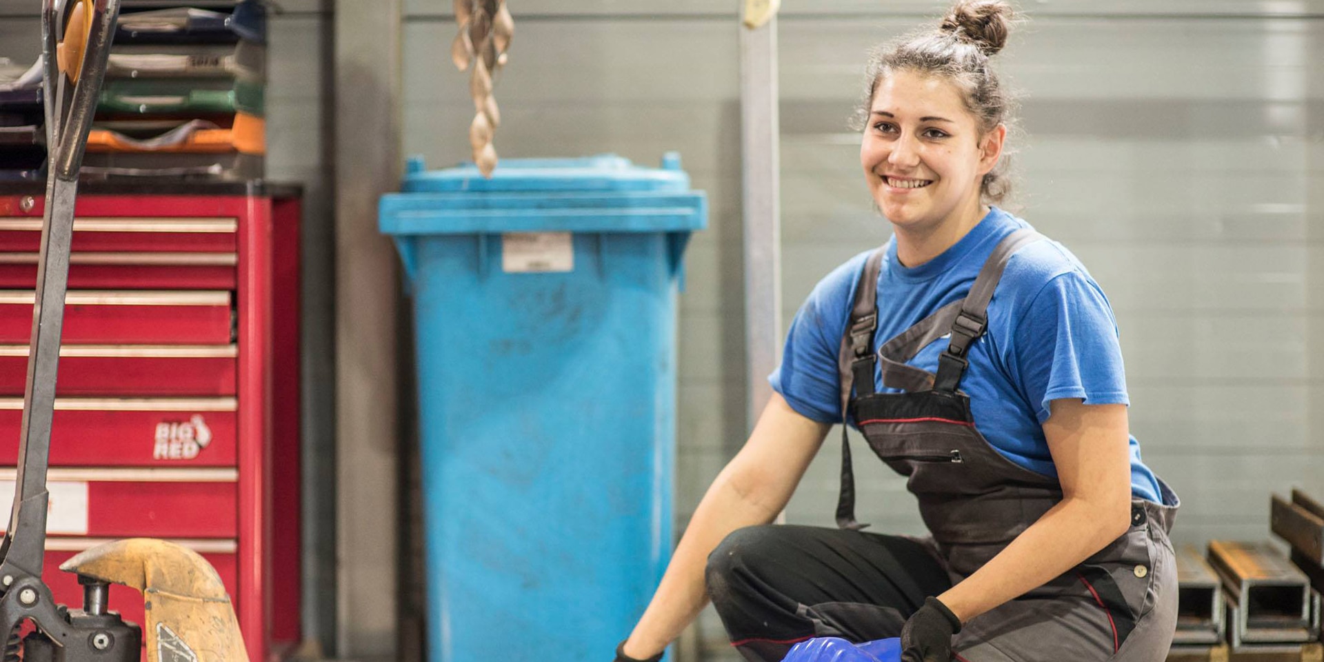  Eine junge Frau in einer Fabrik lächelt in die Kamera.