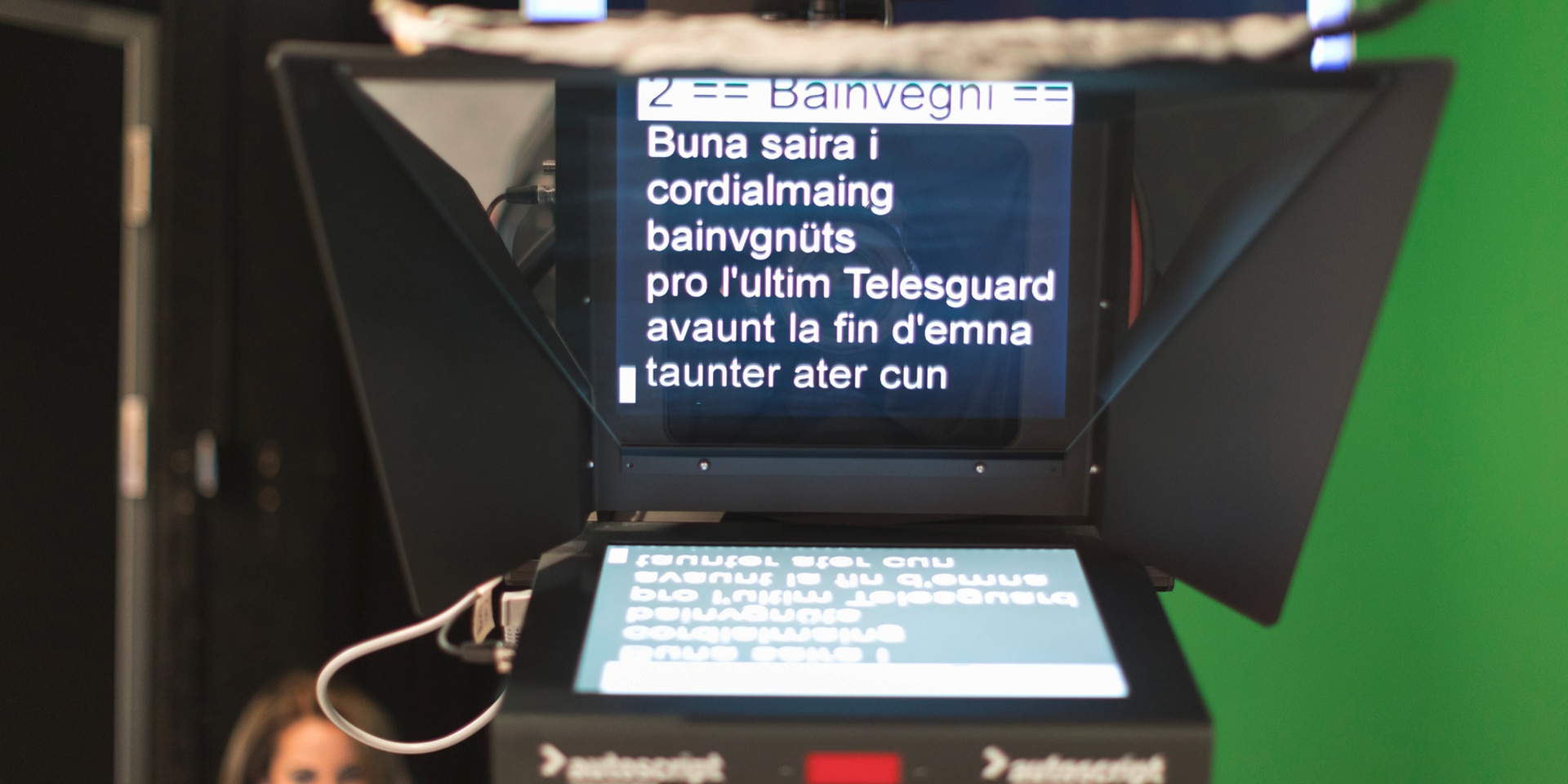 Dans un studio de télévision, un écran affiche le texte du présentateur en romanche.
