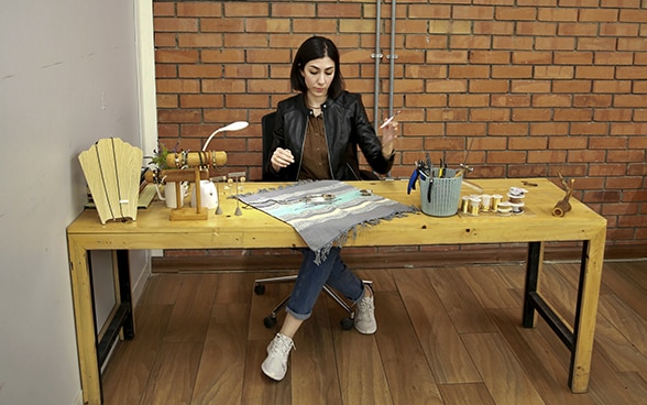 Una giovane imprenditrice irachena seduta a un tavolo di legno realizza gioielli.