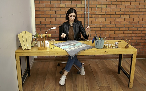 A young Iraqi entrepreneur sits behind a wooden table and assembles jewellery.