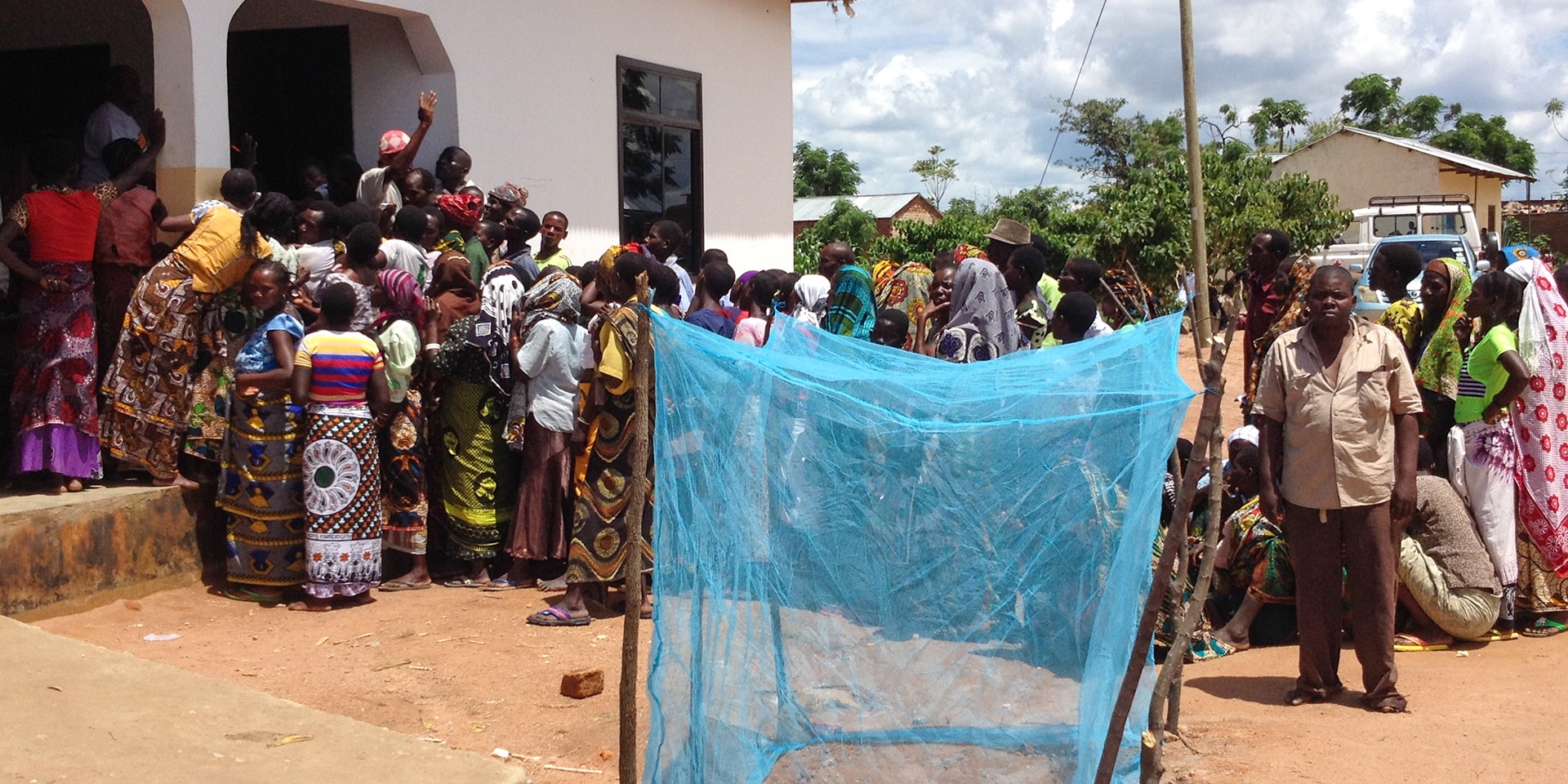 Dans un village de Tanzanie, de nombreuses personnes font la queue pour récupérer des moustiquaires. Au premier plan, on aperçoit une grande moustiquaire bleue.