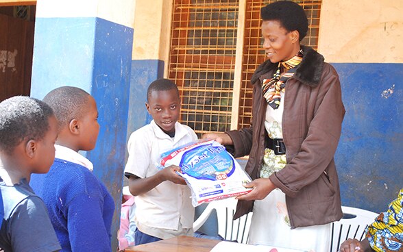 A woman gives a mosquito net to a child. Two other children wait in line.