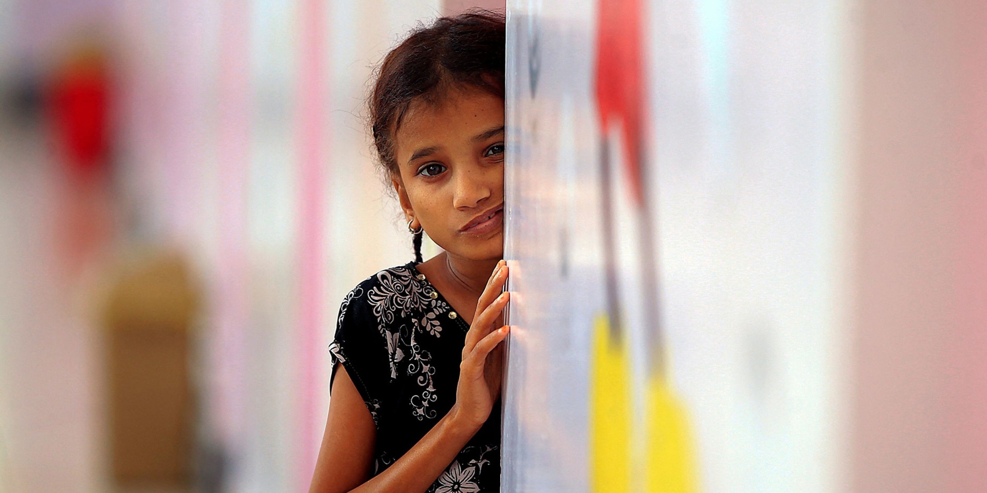 A little girl, with a worried look on her face, is leaning against a wall waiting for food.