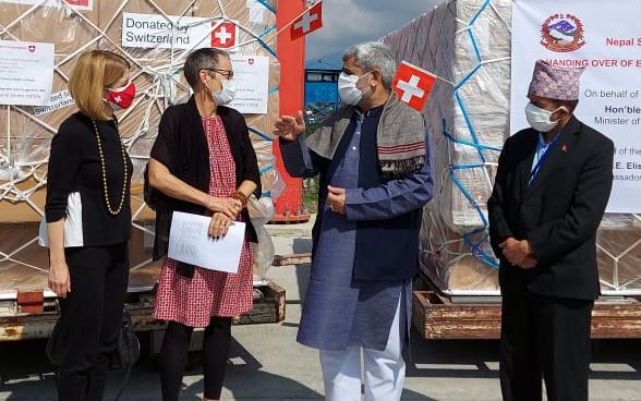 Quatre personnes, dont l’ambassadrice de Suisse au Népal, Elisabeth von Capeller, photographiées devant une palette de matériel de secours sur le terrain de l’aéroport de Katmandou.