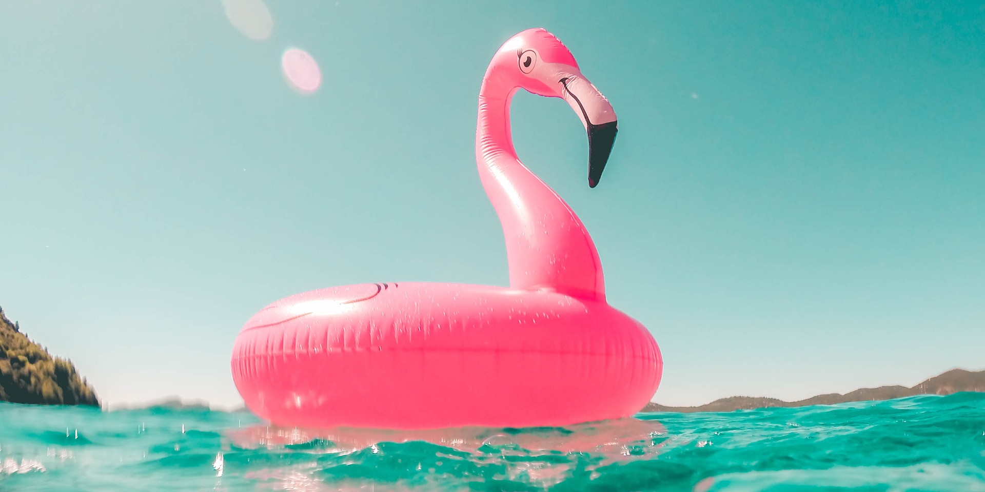 Ein rosaroter, aufblasbarer Flamingo aus Plastik treibt auf dem türkisfarbenen Meer.