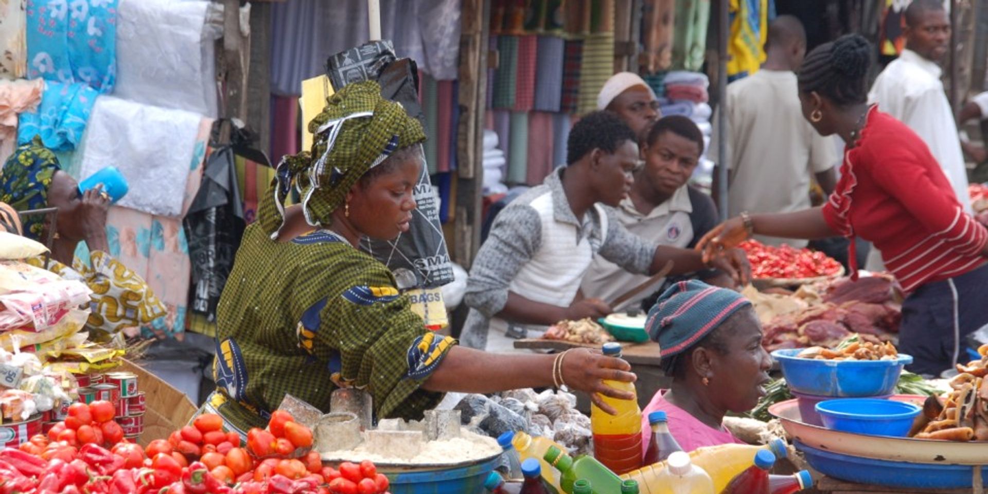 A woman getting a bottle for a customer at a market stall in Africa.