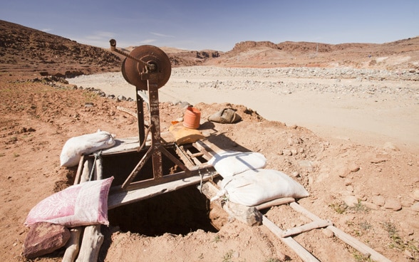 A well next to a dry riverbed in a desert landscape.