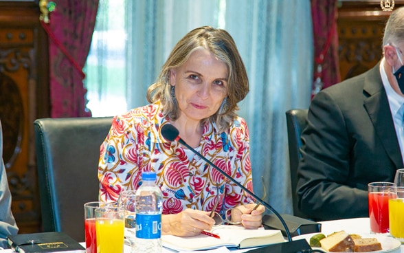 Walburga Roos, souriante, est assise à une table devant un microphone.