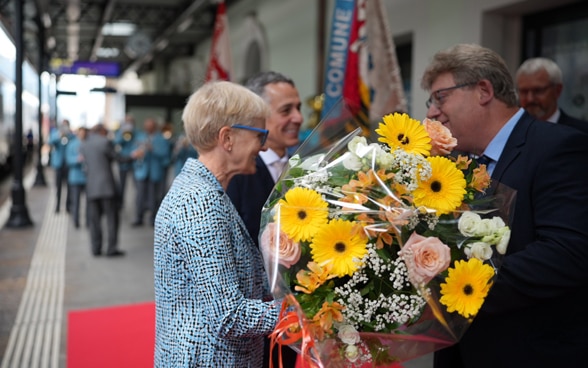 On the platform of the Biasca railway station, Paola Cassis receives a bouquet of flowers from the mayor.