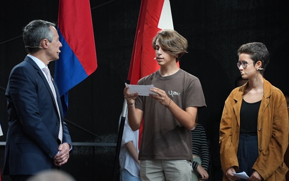 Sur la scène, des étudiantes et des étudiants s’adressent au président de la Confédération Ignazio Cassis.