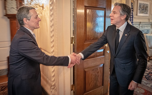 Bundesrat Cassis und US-Aussenminister Blinken gehen aufeinander zu, um sich die Hand zu geben.