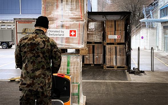A Swiss army member pushes pallets of boxes into a truck.