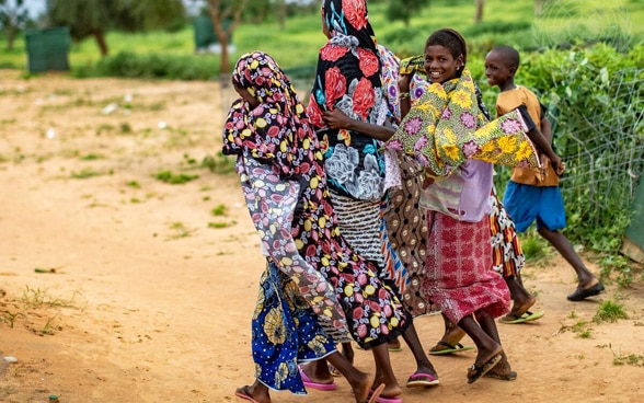 Une femme et des enfants africains marchent sur une route poussiéreuse.