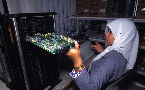 A young girl wearing a veil pulls a motherboard out of a machine.