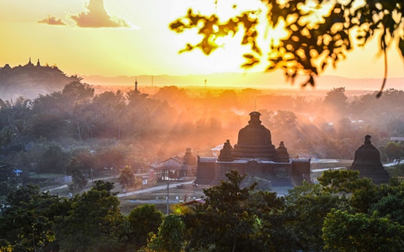 Ein Tempel und ein Haus bei Sonnenuntergang im Nebel im Staat Rakhine in Myanmar.  