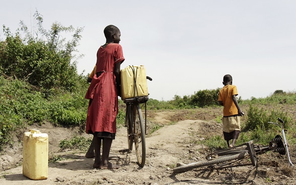 Due bambini di origine africana trasportano lattine gialle in bicicletta.