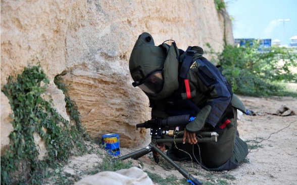 Un homme portant un équipement de protection désamorce un engin explosif.