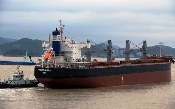 A black and red cargo ship with four chimneys flies the Swiss flag.