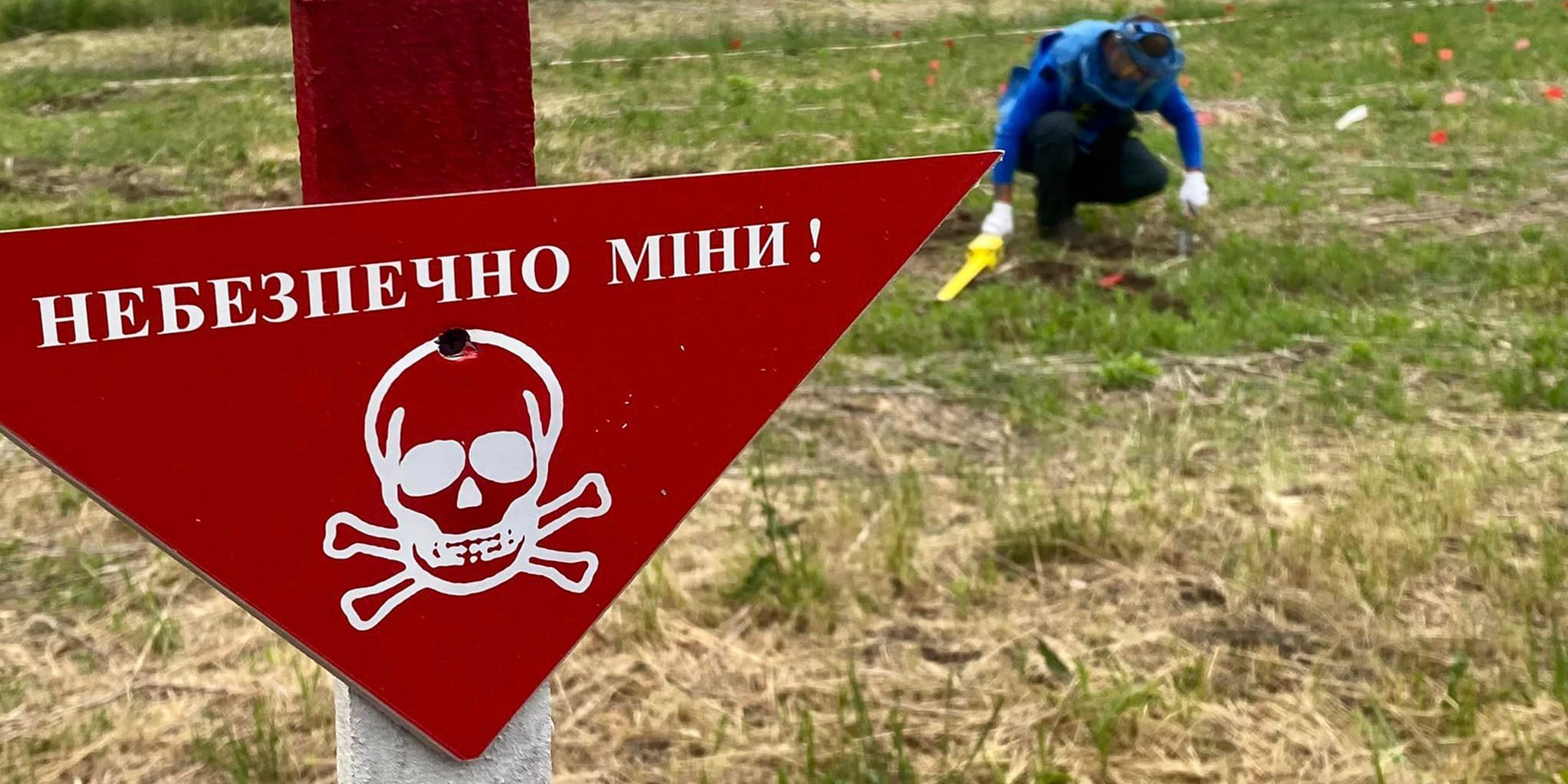 Un uomo in abbigliamento protettivo lavora in un campo con un cartello di pericolo di morte.