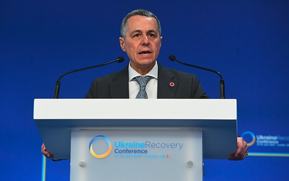 Bundesrat Ignazio Cassis steht an einem Pult und spricht. Auf der Vorderseite des Pults ist das Logo der Ukraine Recovery Conference 2023 zu sehen.