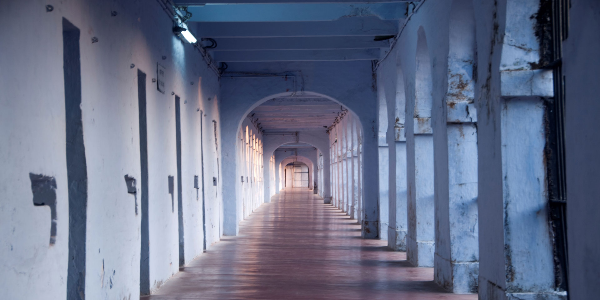 A white corridor lined with cell doors in a prison in India.
