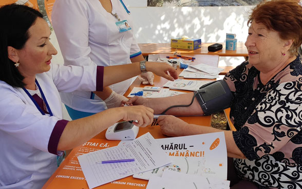 A woman measures the blood pressure of another woman sitting opposite her. 