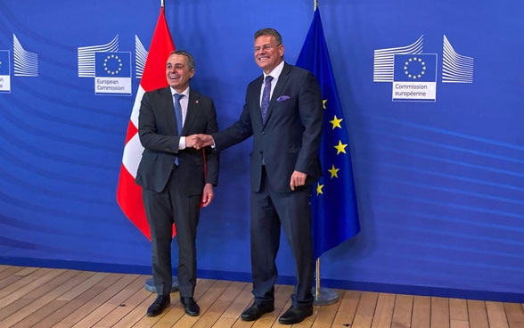 Ignazio Cassis und Maroš Šefčovič schütteln sich die Hände. Die Schweizer und die EU-Flagge sind im Hintergrund zu sehen.