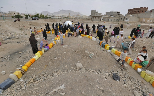 Donne e bambini yemeniti aspettano di riempire delle taniche con l'acqua di una sorgente.