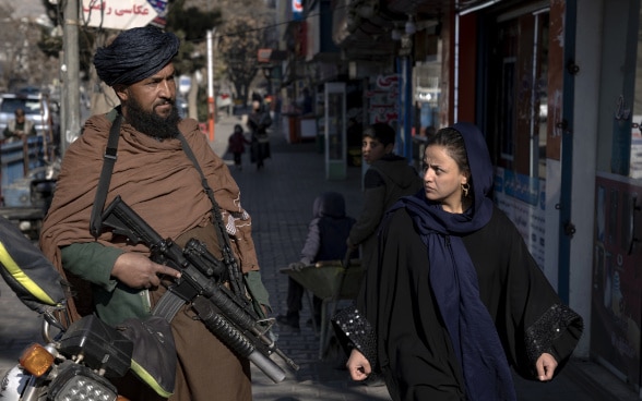 Un combattente talebano fa la guardia mentre una donna gli passa accanto a Kabul.