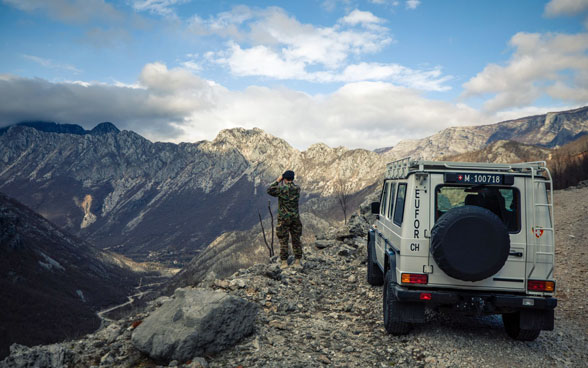 Un membro dell'Esercito svizzero si trova accanto a un veicolo operativo e osserva una valle in Bosnia ed Erzegovina.