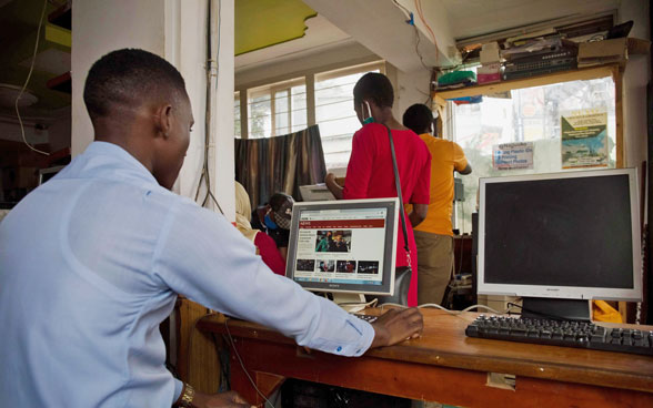 Un uomo africano siede dietro un computer e legge un giornale online.