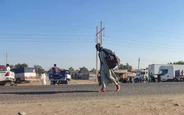 Un homme déplacé à l'intérieur du Soudan marche le long d'une route avec ses affaires.