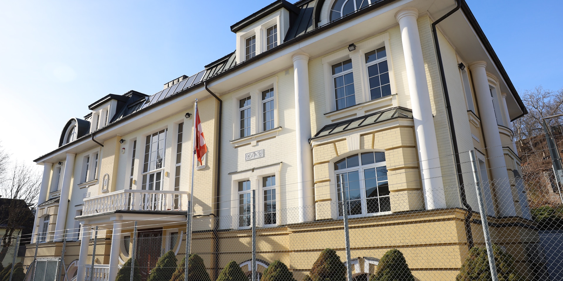 A house with a bright yellow painted façade and a Swiss flag in front of it.