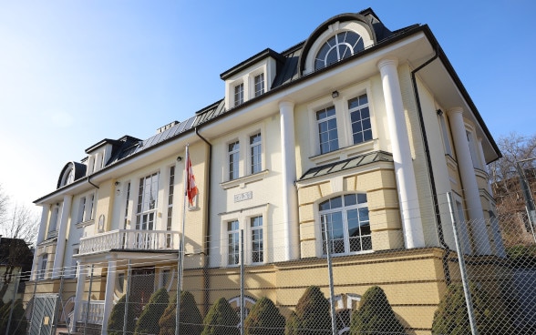 A house with a bright yellow painted façade and a Swiss flag in front of it.