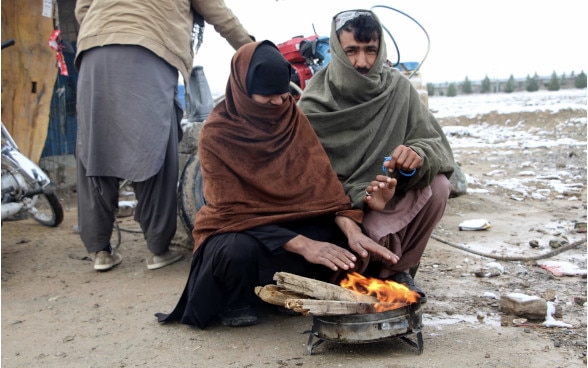 A woman and a man warm their hands by a fire in Afghanistan. The ground is covered in snow.