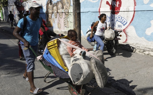 Une famille avec un enfant fuit la violence en Haïti avec ses biens dans une brouette.
