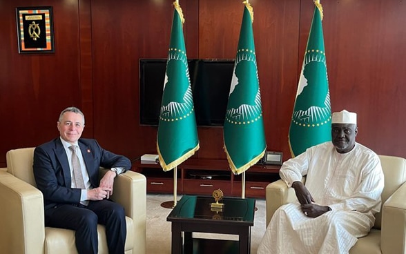 Ignazio Cassis et Moussa Faki Mahamat sont assis sur des fauteuils blancs. 