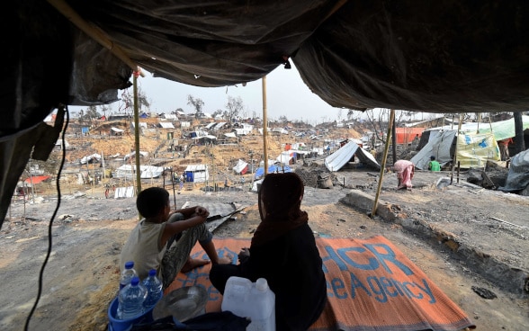 Une femme et un enfant sont visibles sur fond d'abris provisoires mis en place pour les réfugiés rohingyas déplacés.