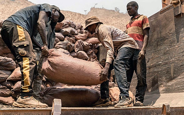 Three people loading bags full of minerals onto a lorry. 